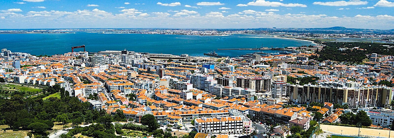 View from above over the rooftops and buildings of Almada, with the Tagus river and the far bank behind