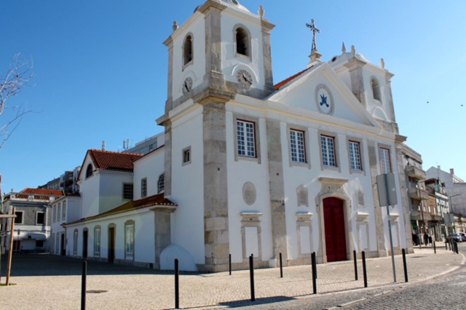 White church with two towers and a red door, on a paved square with black bollards