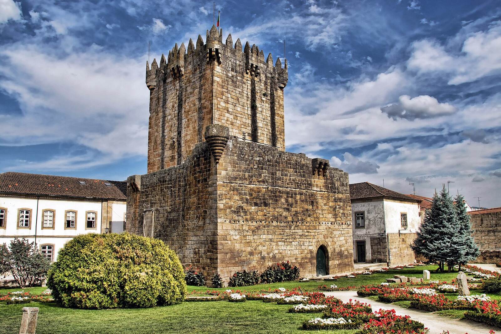 Stone keep of Chaves castle, with a garden and houses around it, under a cloudy sky