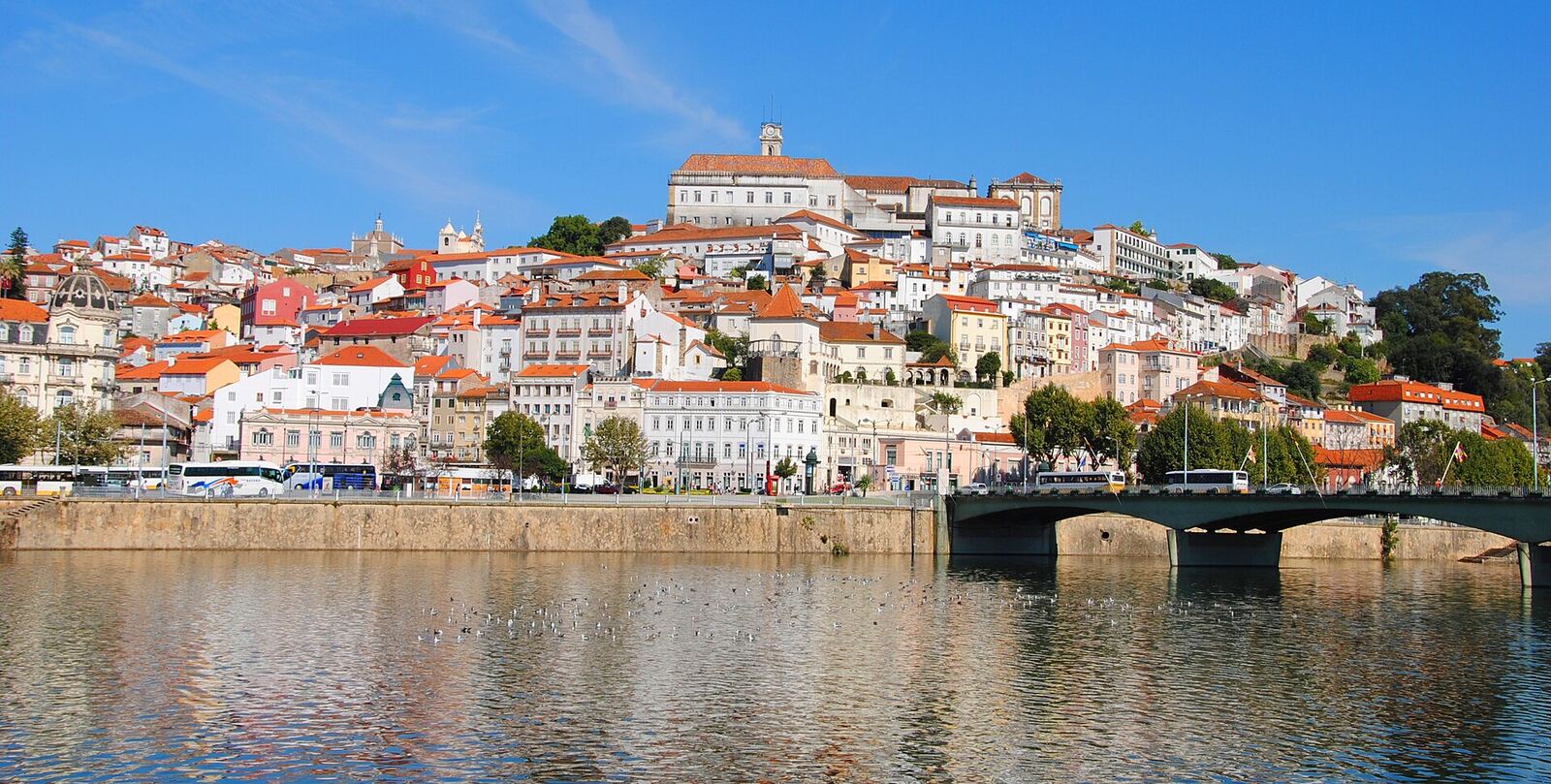 Red-roofed houses climbing a hill, with the Mondego river and a bridge in the foreground