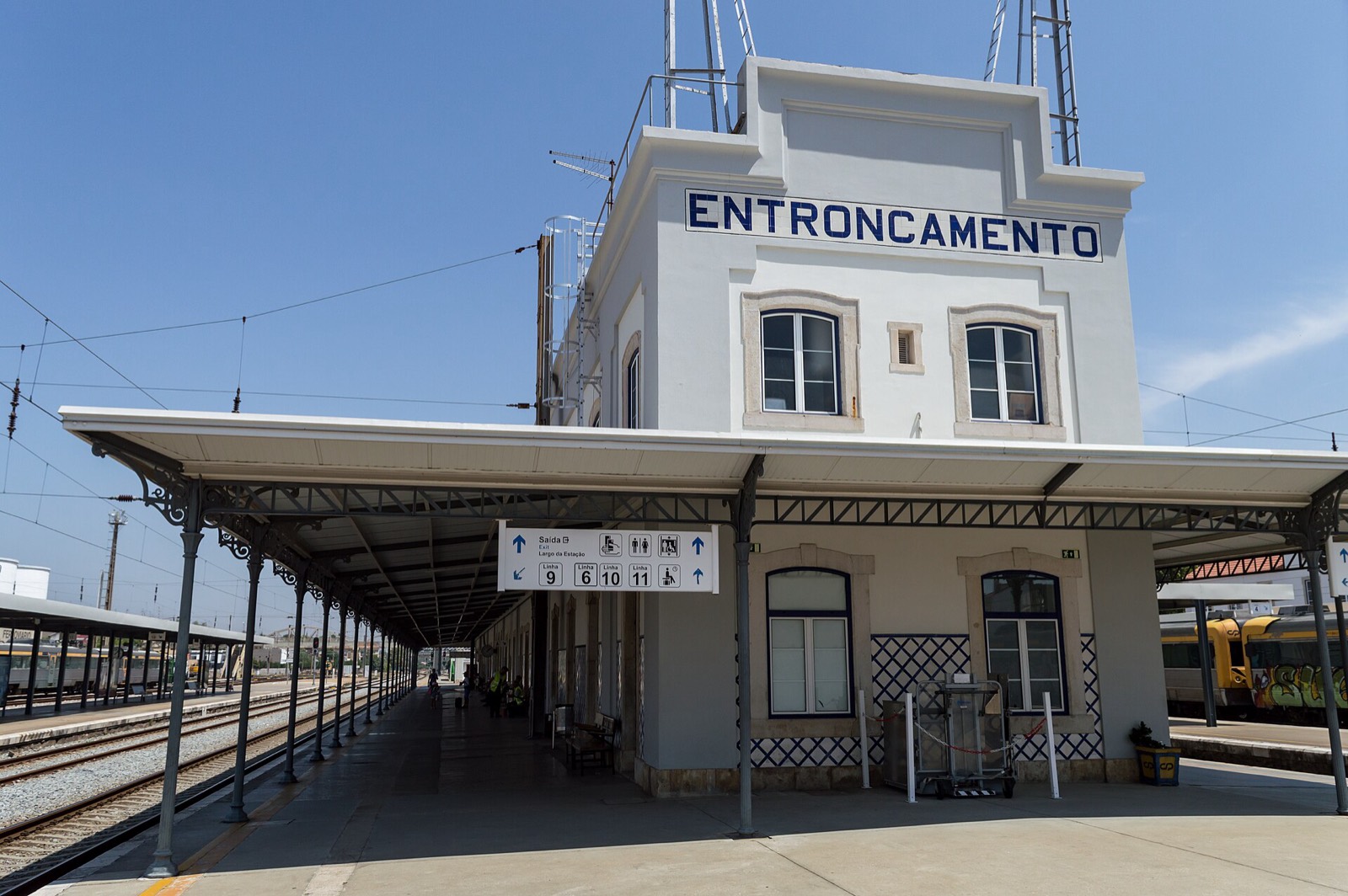 White building of Entroncamento station, with the name in blue letters at the top, and a covered platform with tracks beside it