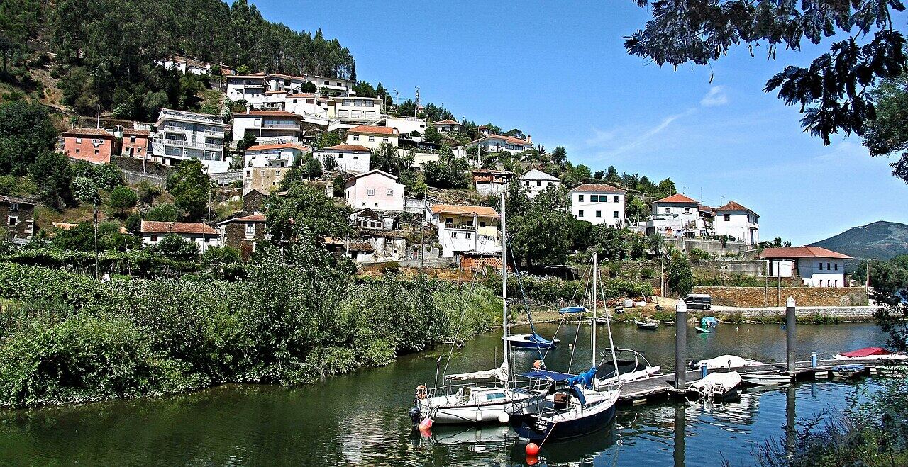Village of white houses on a green hillside by the Douro river, with boats at a quay