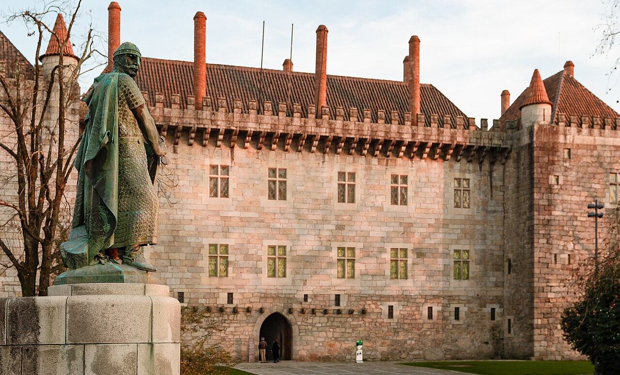 Palace of the Dukes of Braganza, a stone building with tall chimneys, with the statue of King Afonso Henriques in front