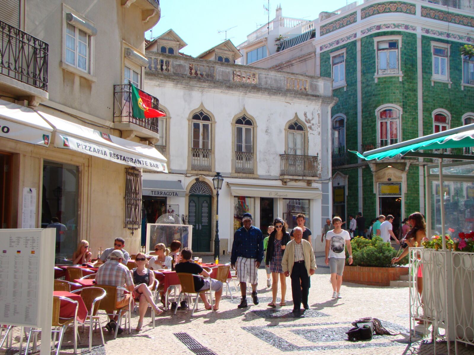 Street in central Lagos with café terraces and old houses, one covered in green tiles