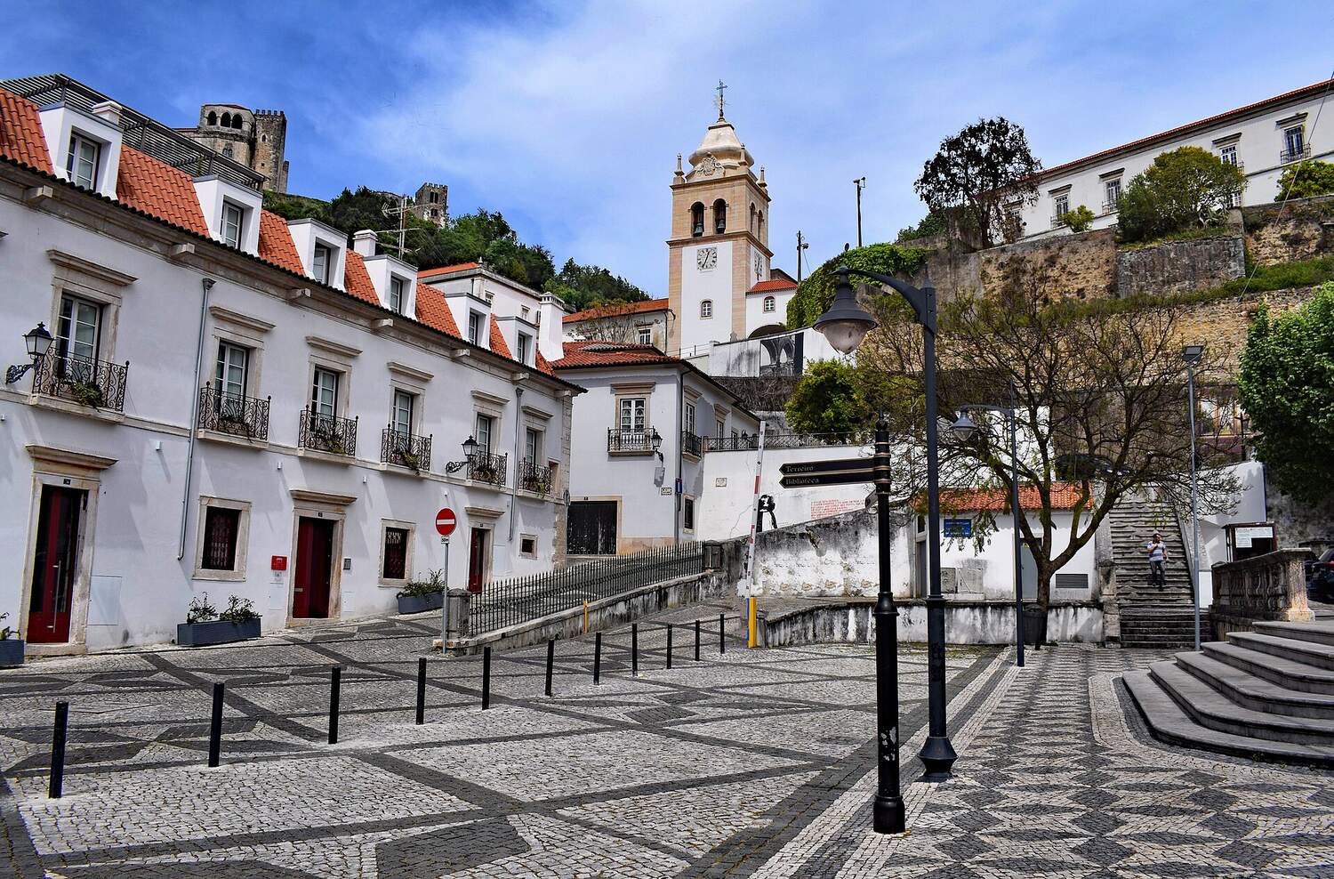 White buildings with iron balconies on a paved square, with a tower in the background