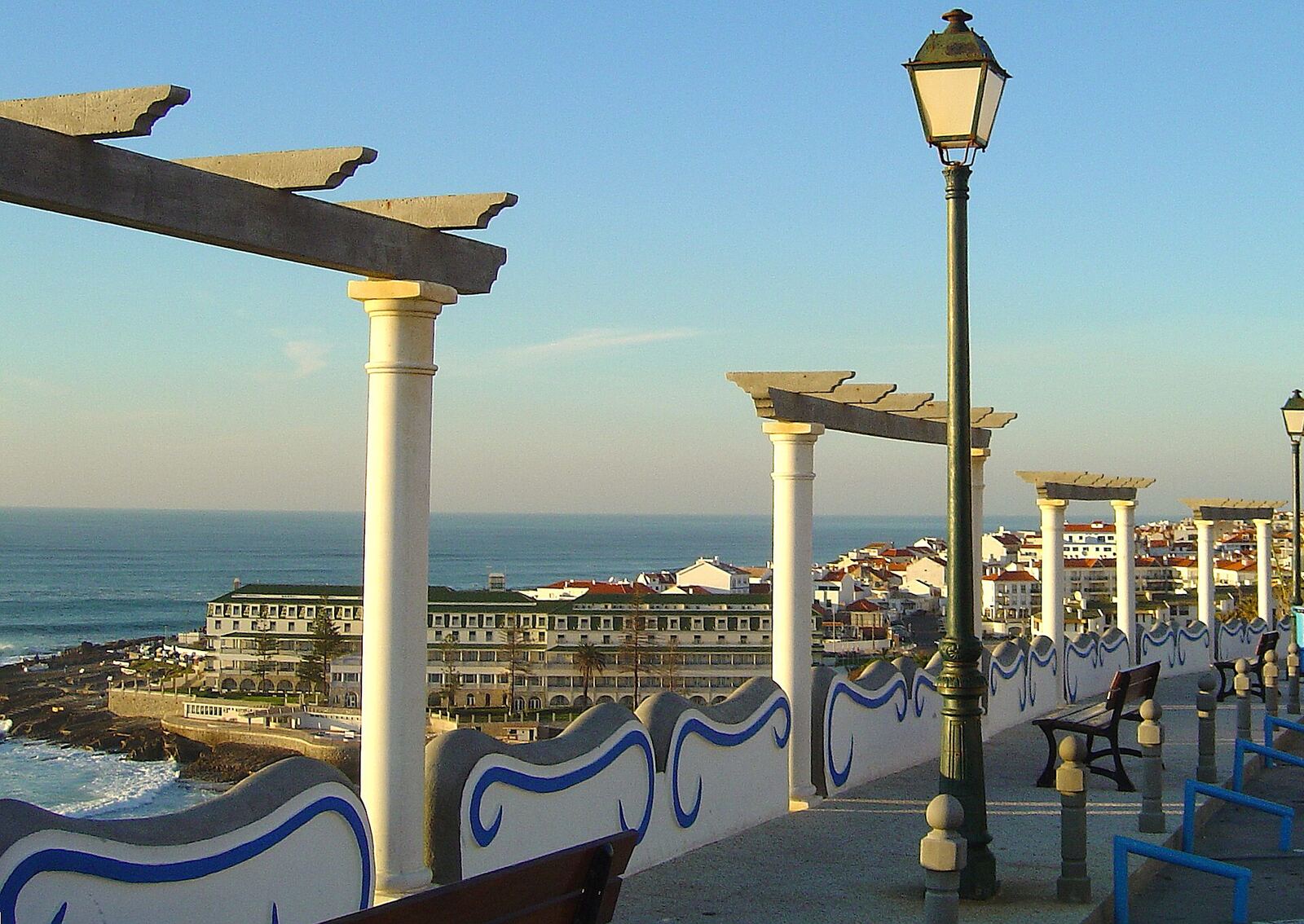 Lookout with white pergolas and street lamps, with the sea and houses of Ericeira behind