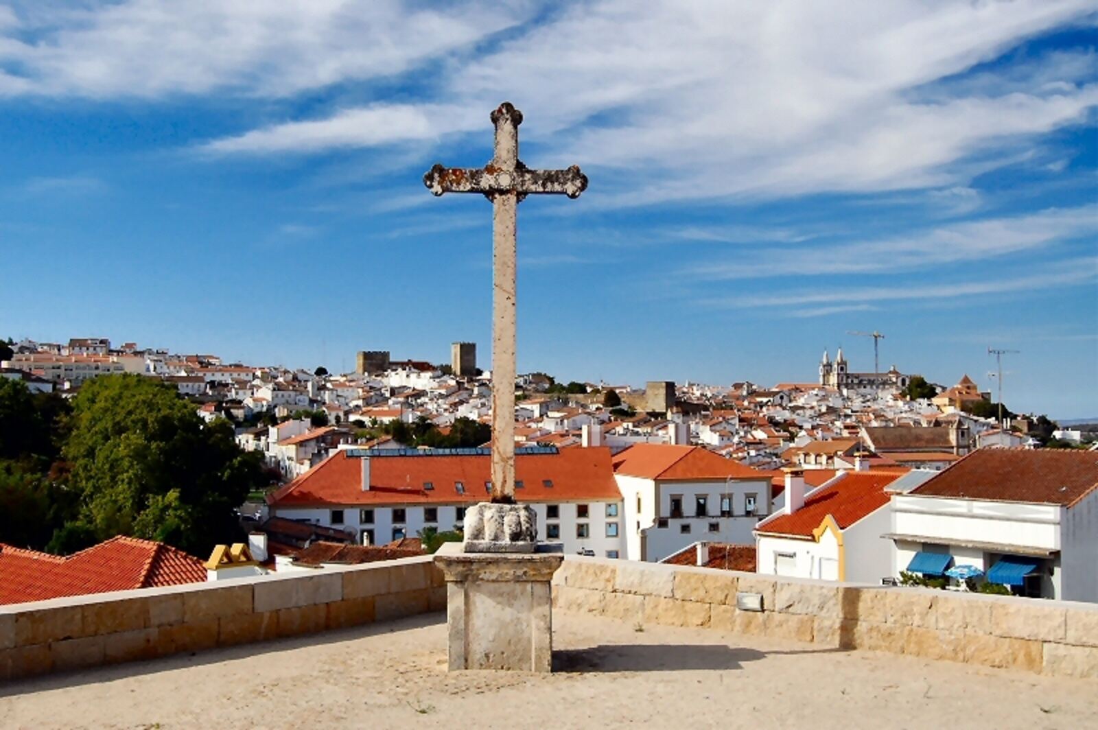 Stone cross in the foreground and, behind it, white red-roofed houses of a hilltop town