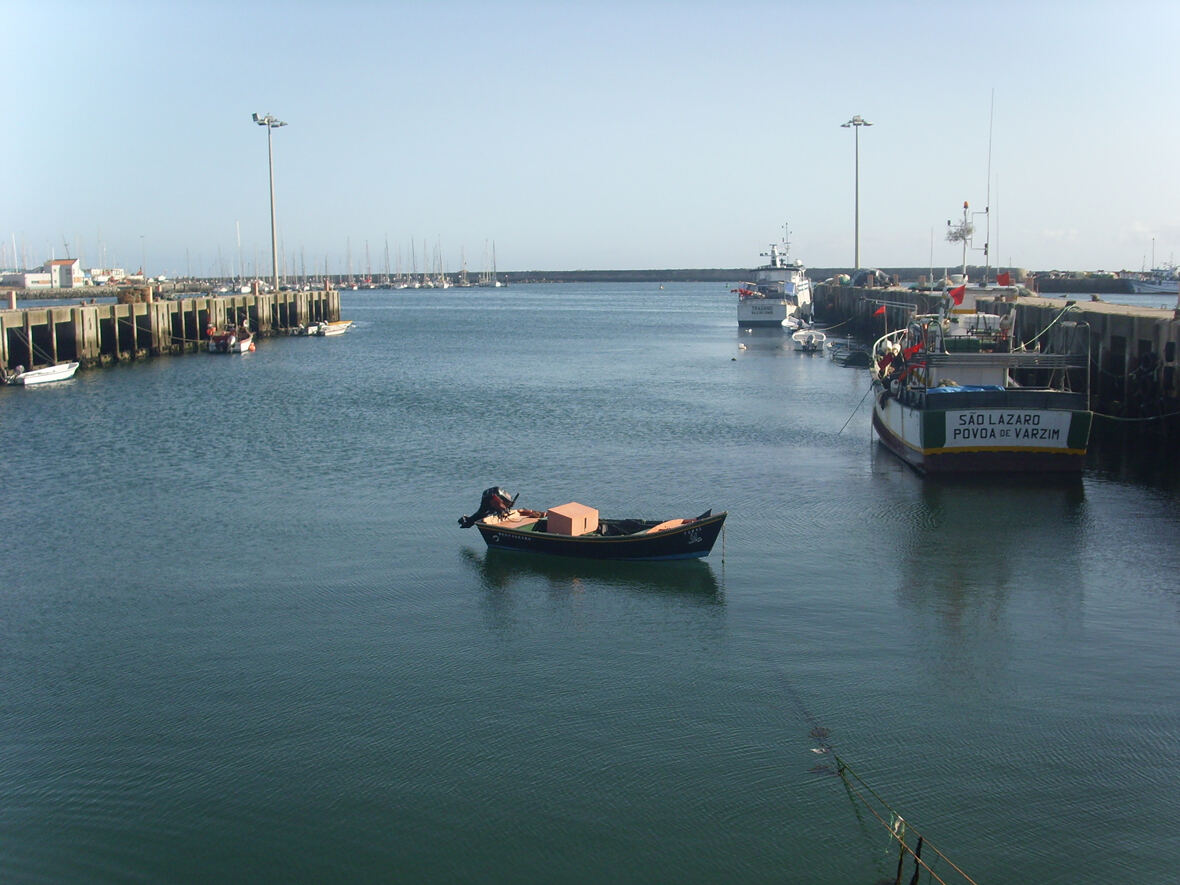 Calm fishing harbour, with a small boat in the foreground and larger vessels at the quay