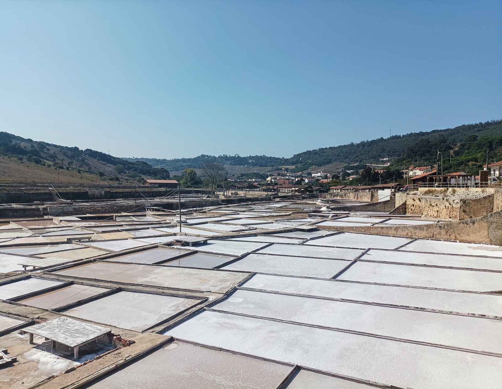 Salt pan basins covered in white salt, with scrub-covered hills behind and houses on the right