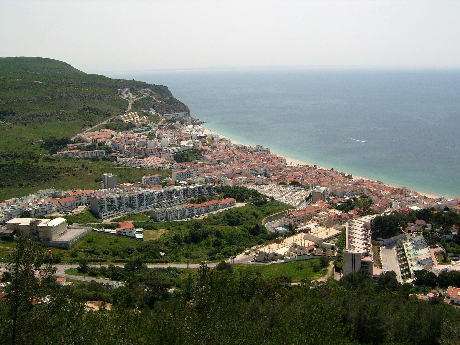 View of the town of Sesimbra, with houses along the beach, a green hillside and the sea