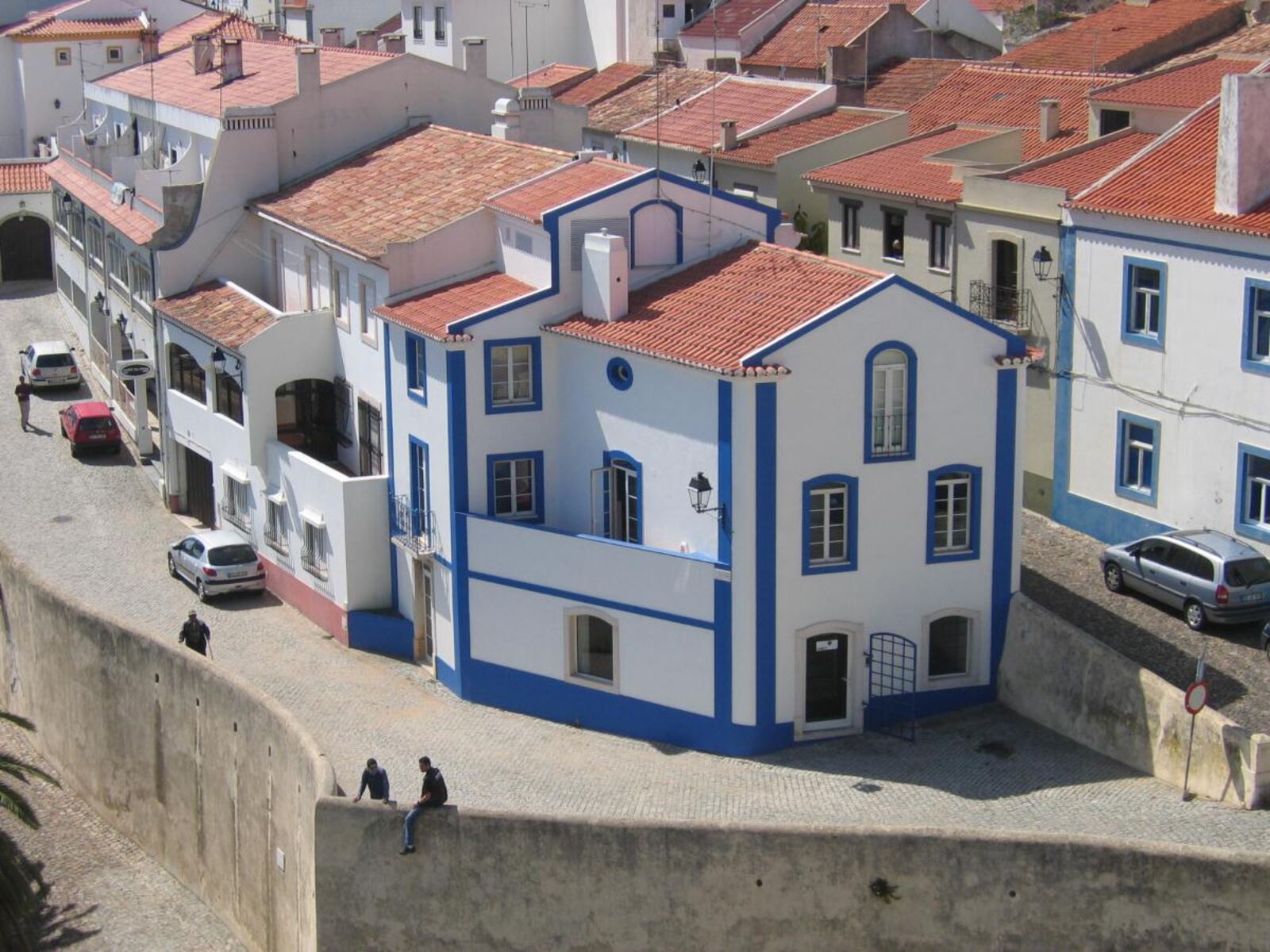 White houses with tiled roofs and blue trim, on a sloping street in Sines