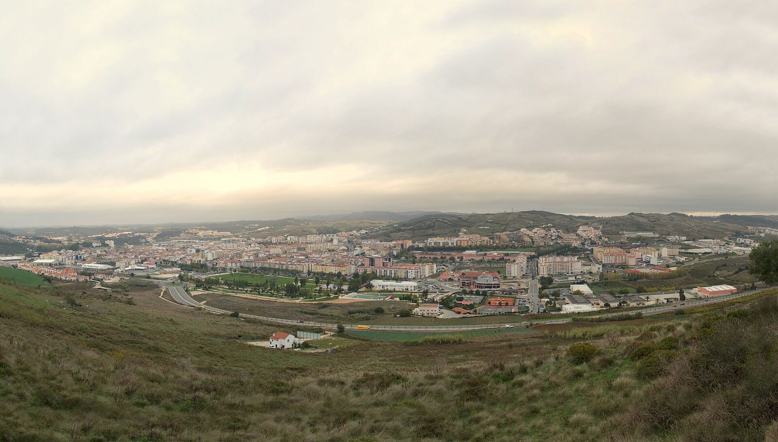 Wide view of a town among green hills, on a day of cloudy sky