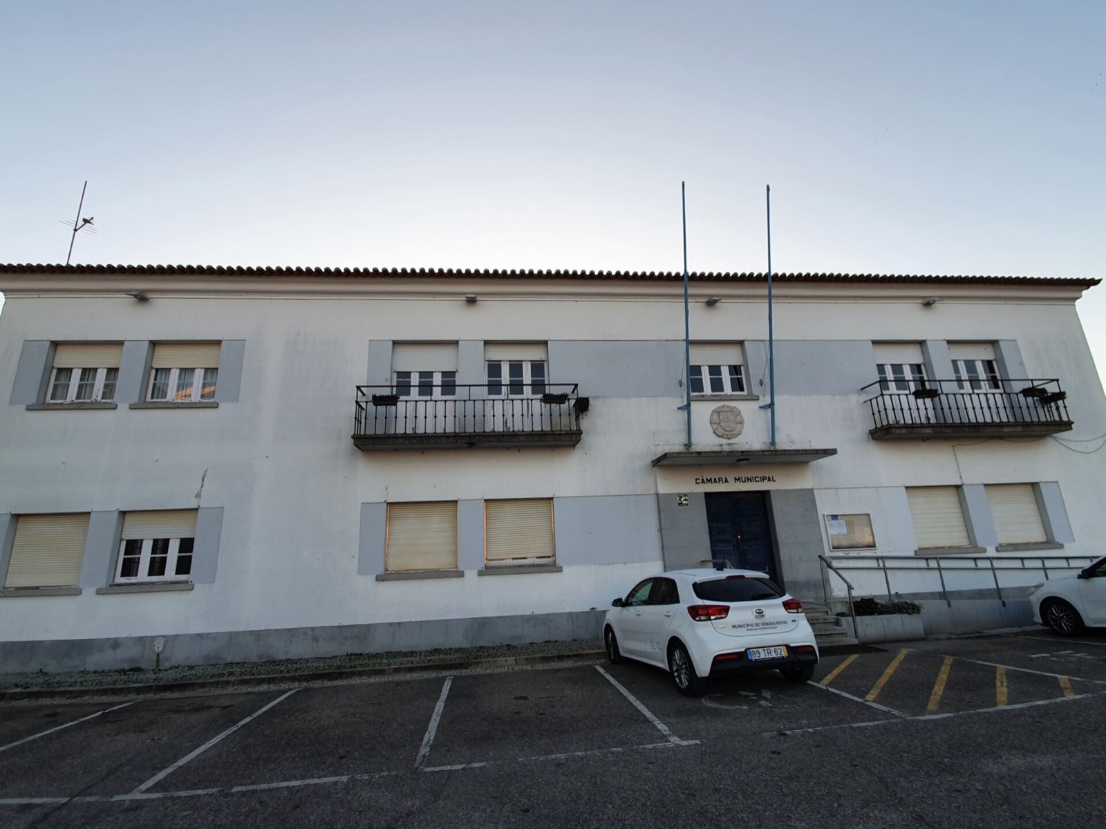 White two-storey building with white-framed windows and roller shutters, two iron balconies and a door with the sign Câmara Municipal