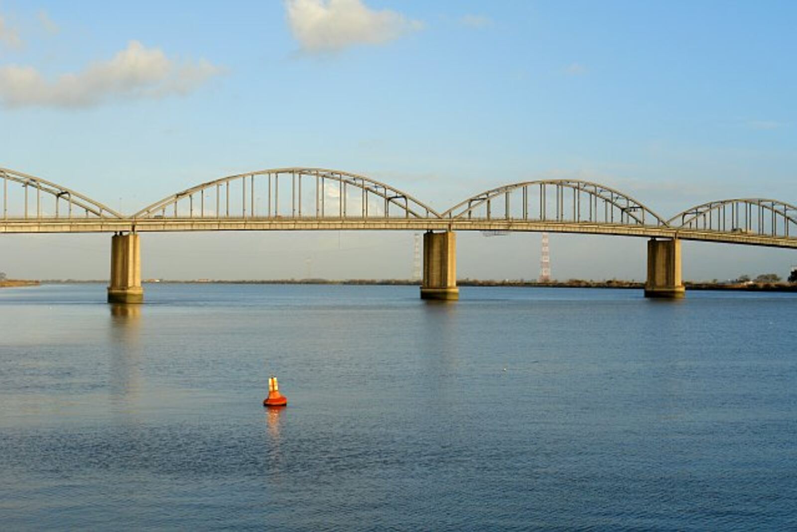 Bridge with metal arches over the Tagus river, with calm water and an orange buoy