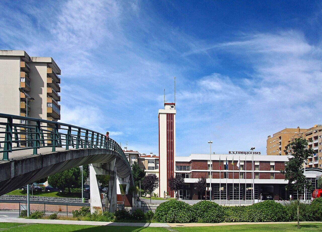 Park with a lawn, a footbridge with green railings and a building with a tower behind