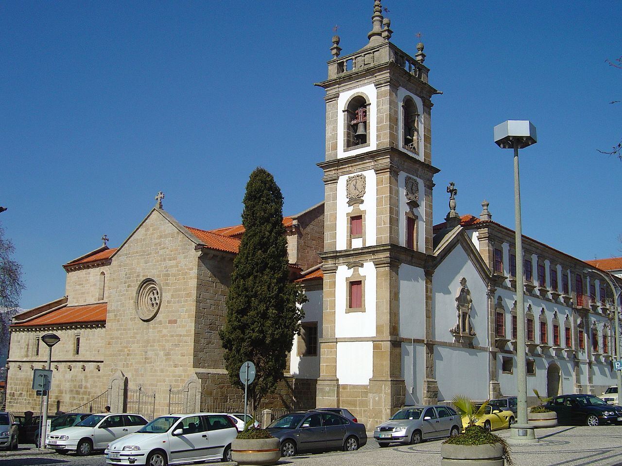 Stone church with a bell tower, surrounded by houses, on a street with parked cars