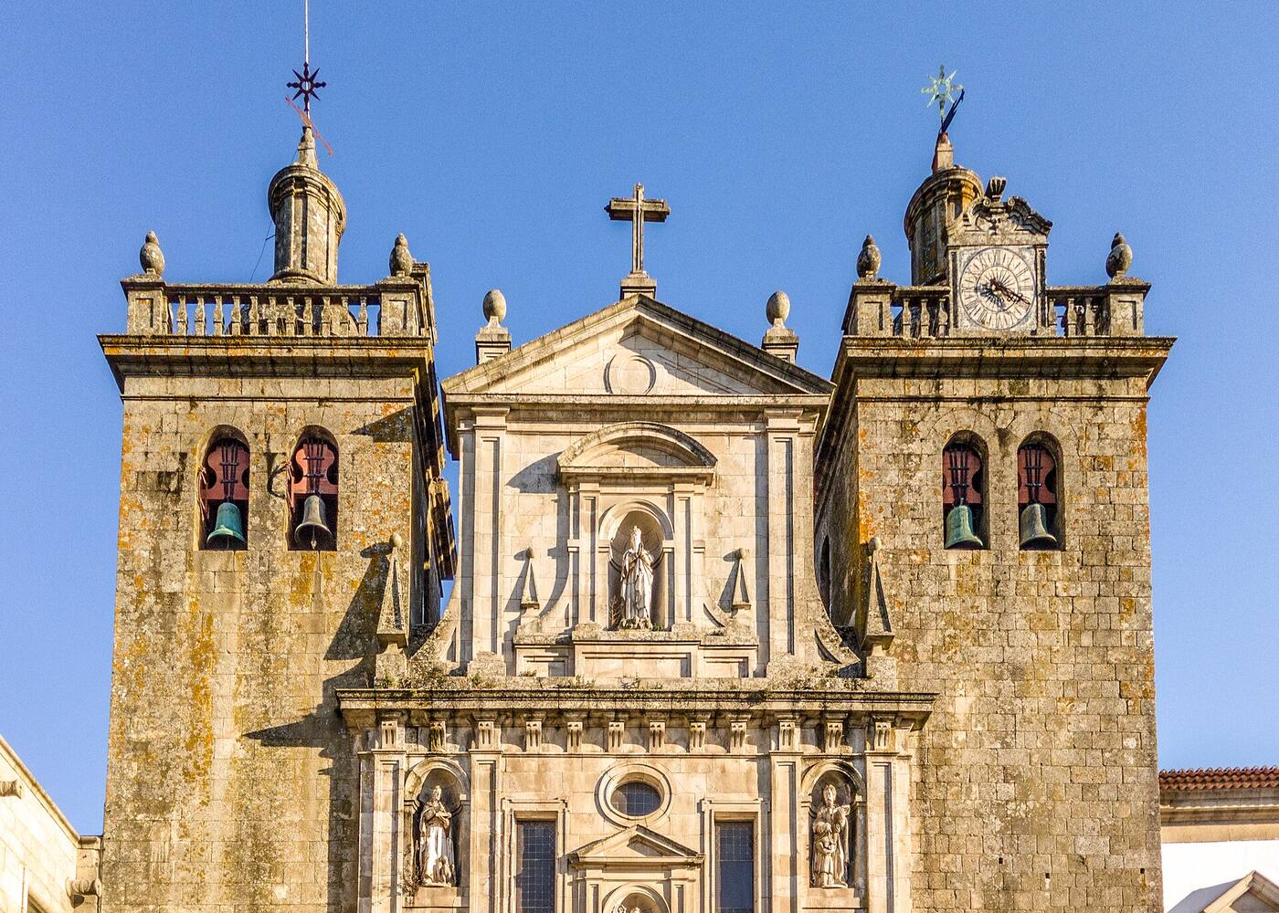 Granite facade of a baroque cathedral, with two bell towers and a clock, against a blue sky