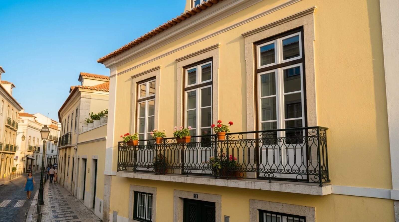 Yellow facade of an old building with tall windows and an iron balcony on a cobbled street